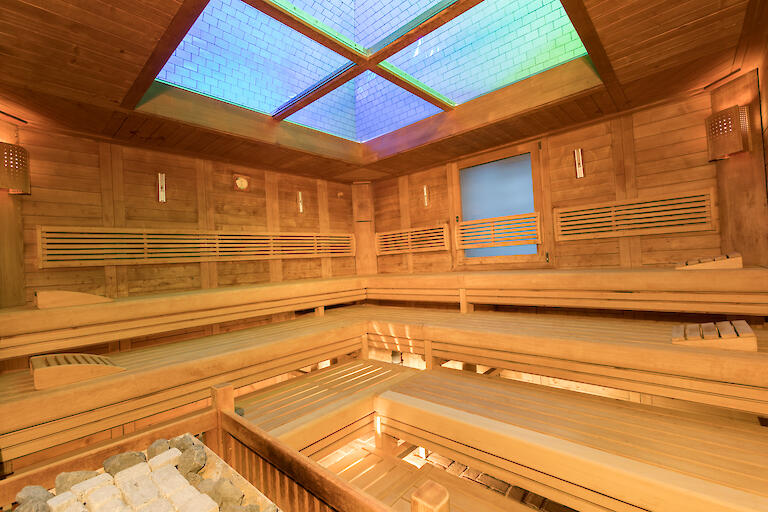 Finnische Sauna mit Holzbänken und einer Glasdecke die beleuchtet ist.