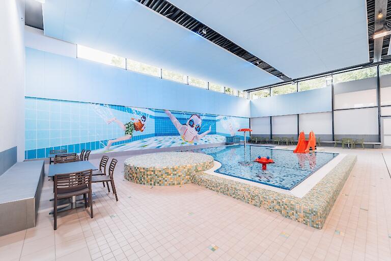 Planschbecken mit Rutsche sowie Tische und Stühle neben dem Becken.